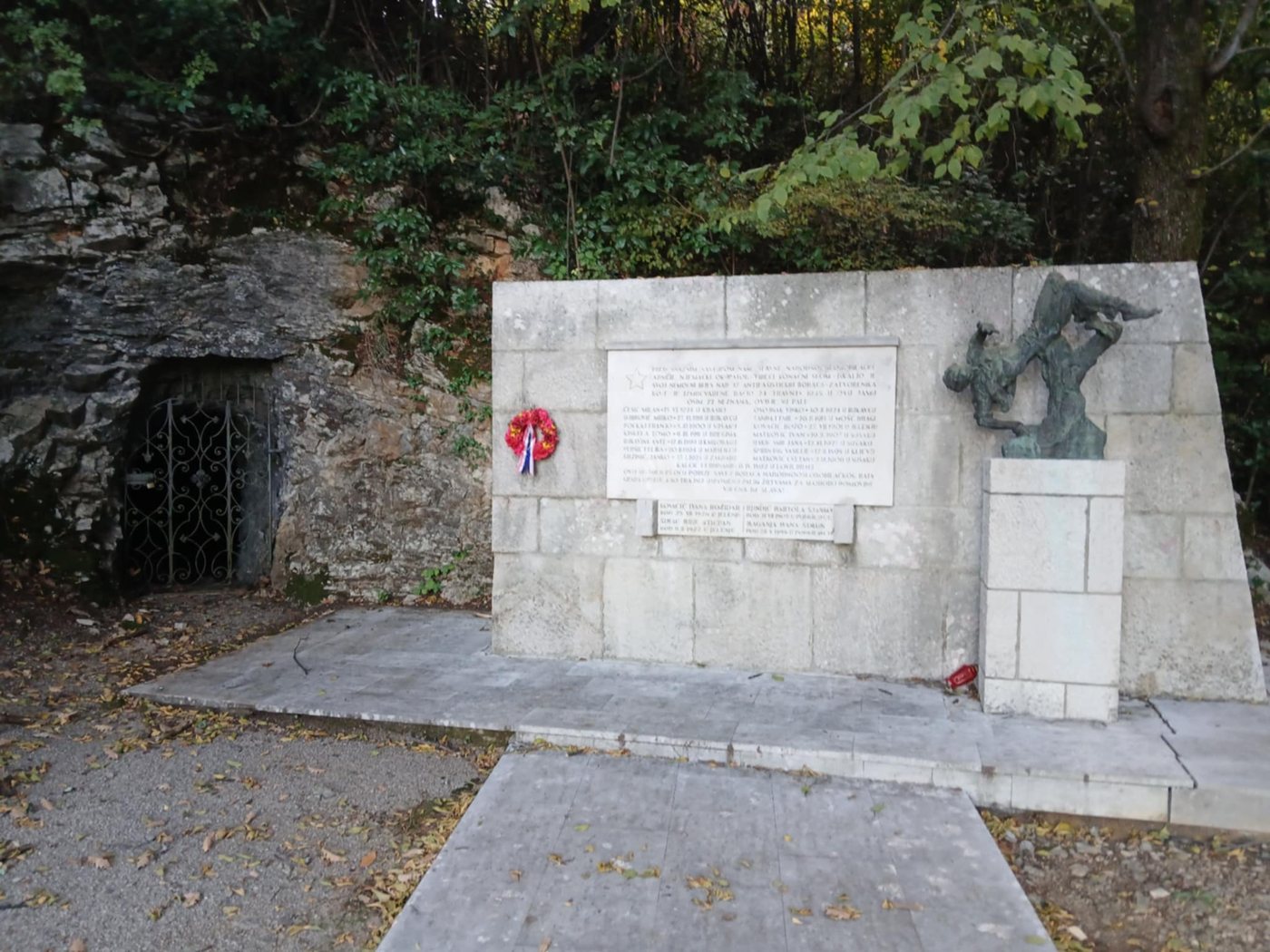 Stone memorial with a bronze sculpture beside a cave entrance near Opatija