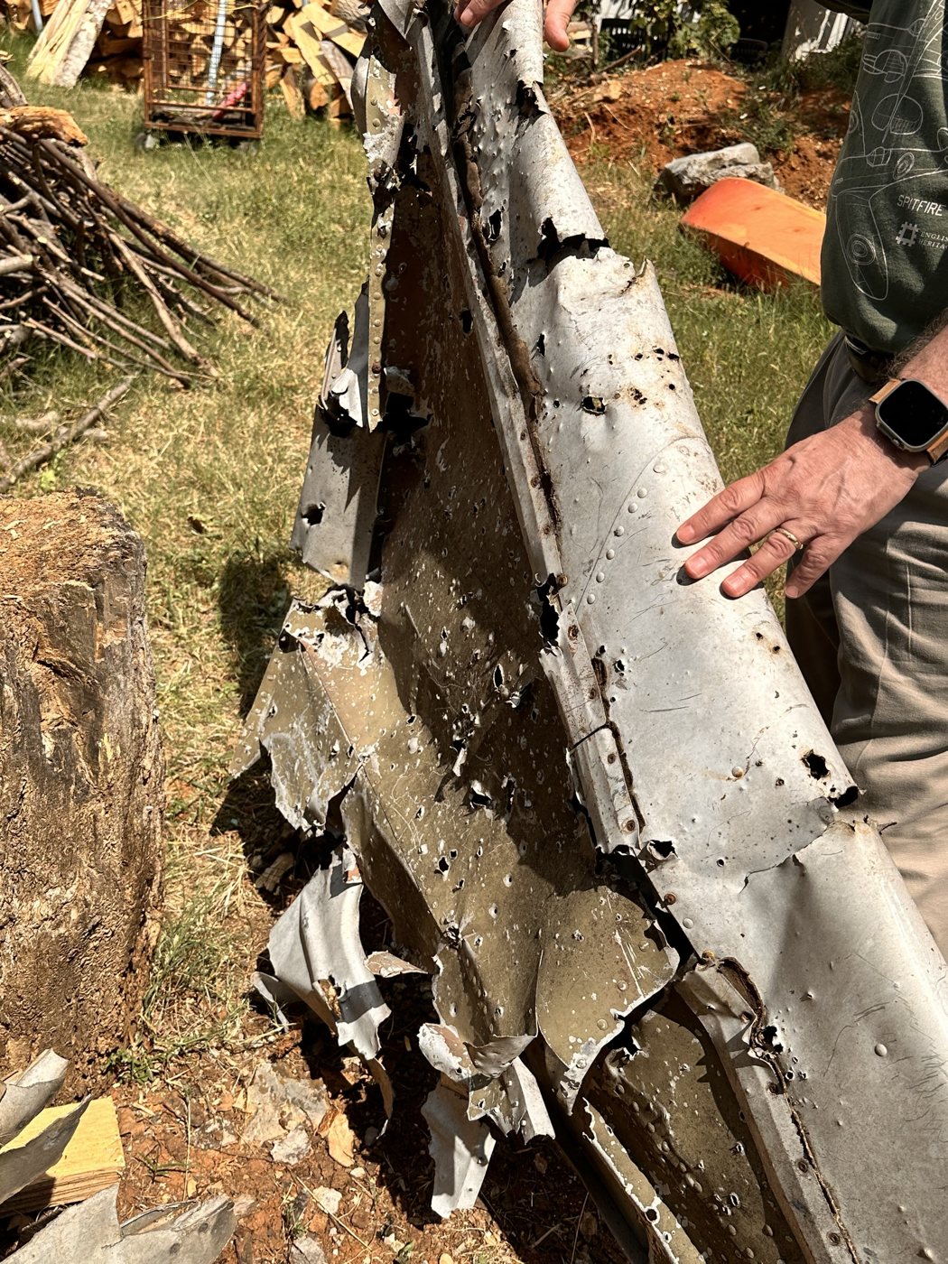 A hand resting on a large, torn section of B-17 aluminum skin among recovered wreckage